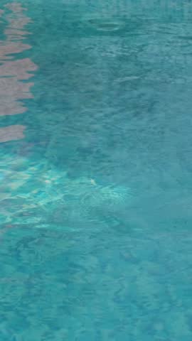 Blue water in a swimming pool with building reflections and visible mosaic tiles at the bottom. Gentle ripples create a dynamic play of light and color
