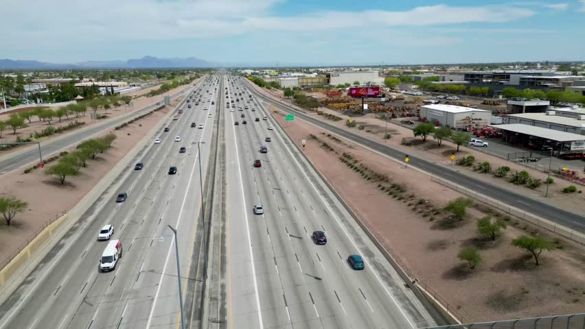 An aerial daytime view of a wide multi-lane highway in Phoenix, Arizona, with steady traffic and desert terrain