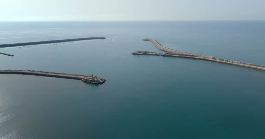 Aerial view of the mouth of a port. The sea extends to the horizon in a backlight.