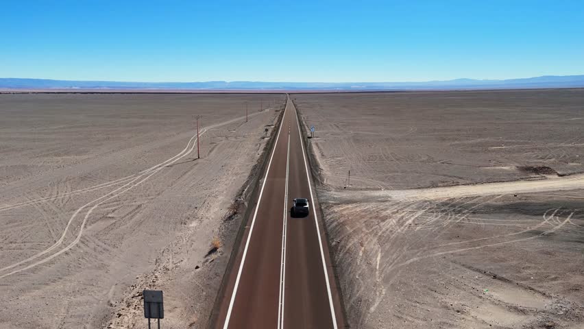 A drone footage of a car driving on a road cuts through Chile's Atacama Desert near San Pedro de Atacama on a clear sunny day