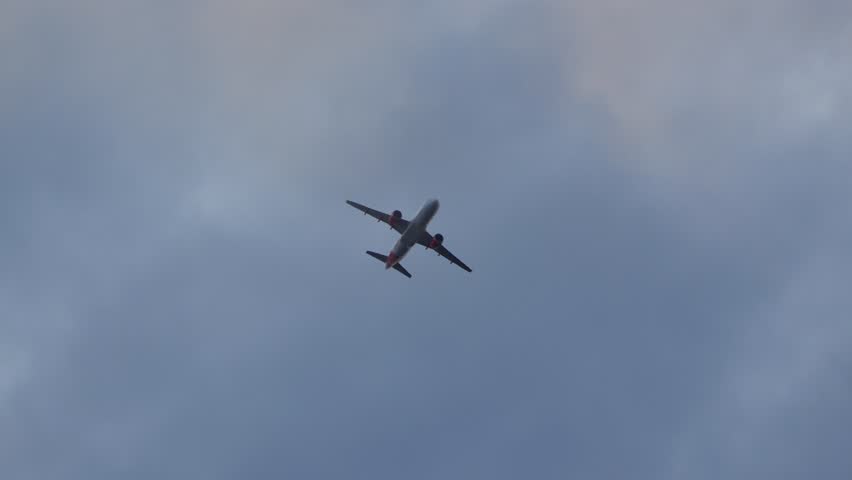 A commercial airplane captured from below flying through a cloudy sky in soft evening light