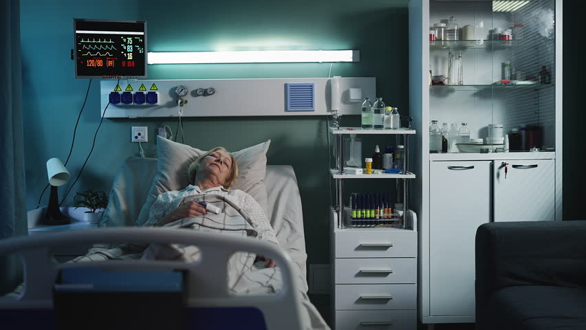 Weak senior woman patient lying in ICU bed with monitor showing vital signs
