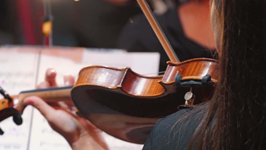 A close-up of a violin in the hands of a musician, demonstrating exquisite skill. The violinist plays the instrument from the rear