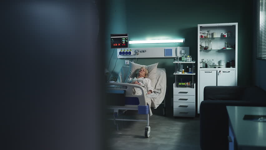 Senior woman patient lying in hospital bed, vital signs visible on ICU monitor