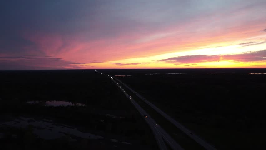 A drone view of a busy highway under vibrant colorful sky at dusk