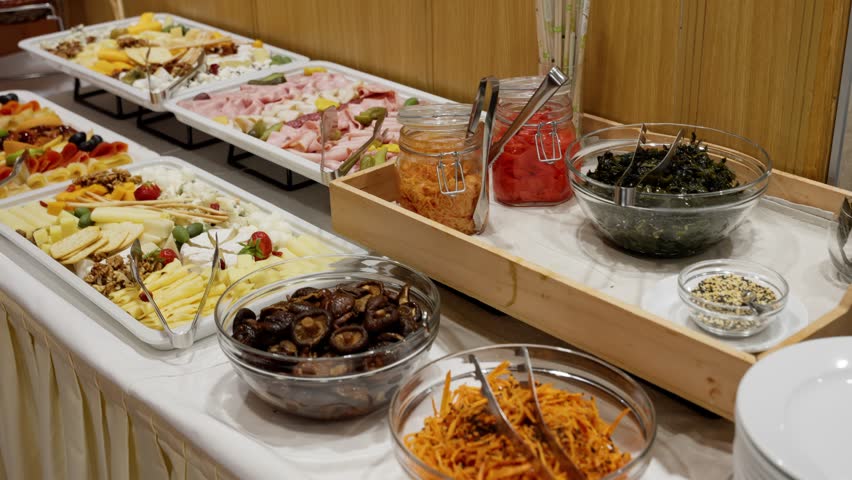 Abundant cold buffet showcasing assorted cheeses, sliced cold cuts, pickles, olives, nuts, fresh fruits, and vibrant salads, arranged on elegant trays with tongs and jars of flavorful condiments