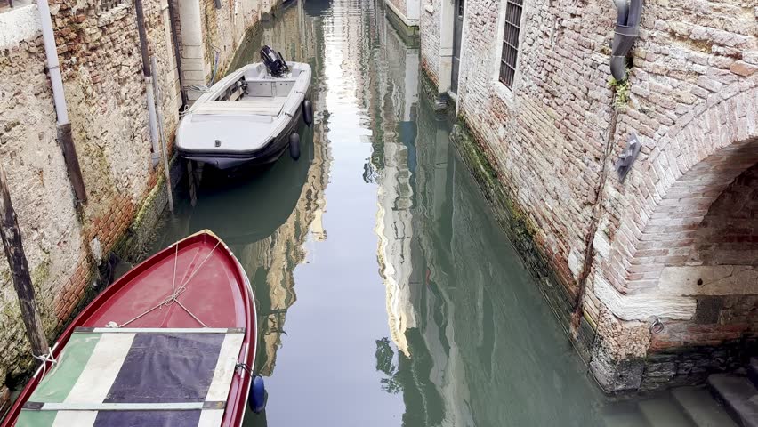 The boats moored on a narrow water canal between the old buildings near Ponte Raspi on a sunny day in Venice, Italy