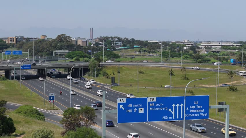 An aerial view of cars driving on Observatory Road under a bridge, with urban greenery surrounding and road signs in Cape Town, South Africa