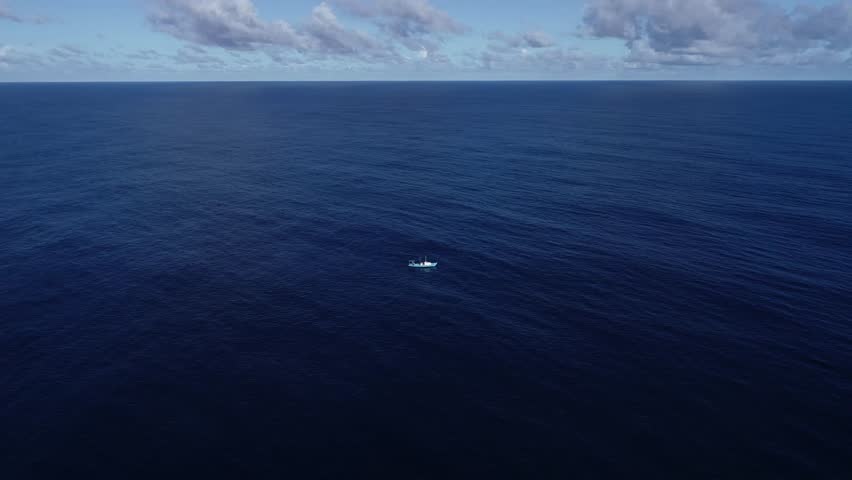 An aerial view of a boat in the middle of vast blue sea water under dramatic cloudy sky