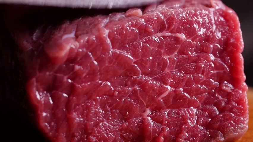 Closeup of Knife Cutting Raw Meat on a Cutting Board