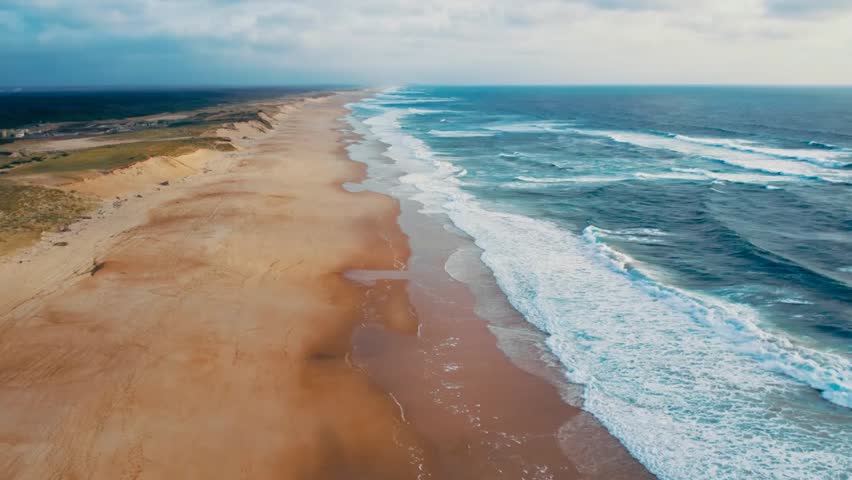 Dolly zoom over stormy ocean shoreline, low tide waves hitting sand dunes under a dramatic cloudy sky.