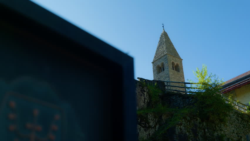 Close-up detail of three crosses and the bell tower of a small mountain church standing on a grassy hill in nature.
