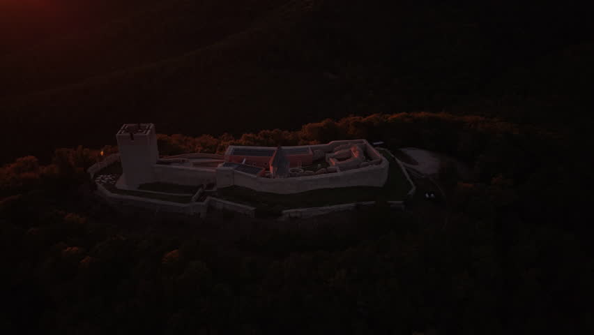 Aerial drone orbit around Medvedgrad fortress during vibrant red sunset with lens flare, Zagreb, Croatia