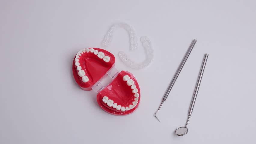 Dental model with dental tools and clear aligners on white background, top view.