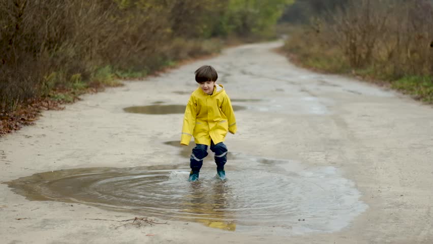 Happy child in a yellow raincoat jumping in puddles on a rainy autumn day in the park.