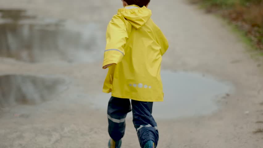 Happy child in a yellow raincoat jumping in puddles on a rainy autumn day in the park.