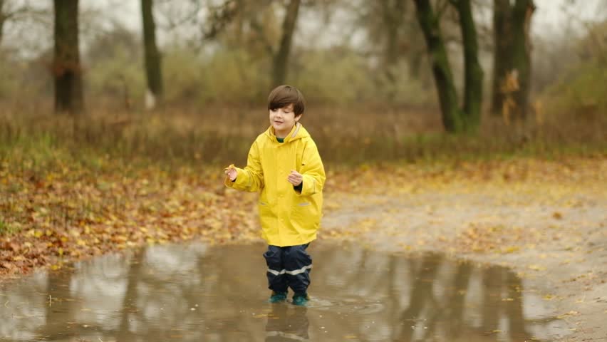 Happy child in a yellow raincoat jumping in puddles on a rainy autumn day in the park.