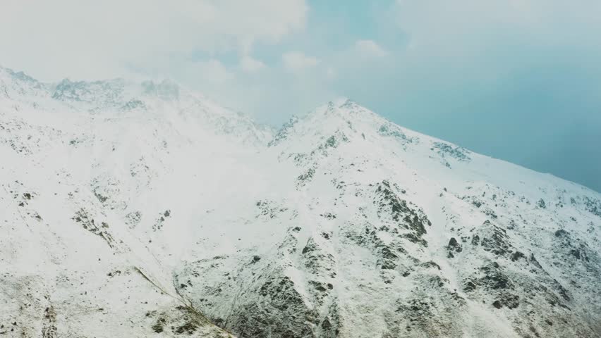 aerial shot of a majestic, snow capped mountain range in the North Caucasus region of Russia. The footage captures dramatic, stormy clouds moving across the peaks, creating a powerful and moody atmosp