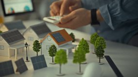 A design engineer uses a calculator while examining a small model of homes equipped with solar panels. This scene takes place in a workspace focused on renewable energy solutions - Powered by Shutterstock - Get 15% off with code: PIKWIZARD15