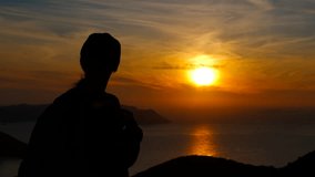 Hiker silhouette watching golden sunset over calm ocean. Silhouetted lone hiker overlooking golden sunset illuminating serene ocean waters against mountain landscape during tranquil evening - Powered by Shutterstock - Get 15% off with code: PIKWIZARD15