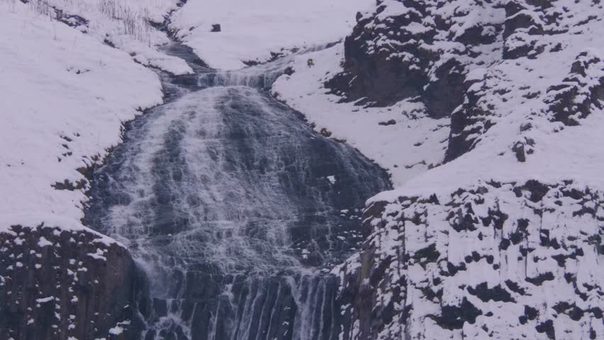 A view of a powerful waterfall cascading down a snow covered mountain slope in the rugged and beautiful North Caucasus region of Russia.