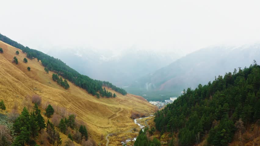 A beautiful, wide angle shot of a mountain valley in the North Caucasus region of Russia. The footage shows a winding river flowing through a valley flanked by steep hillsides covered in golden grass