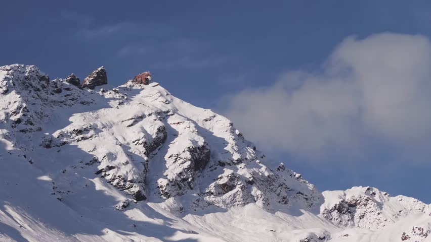 A winter landscape of the North Caucasus mountains in Russia. The footage captures a snow covered peak under a clear blue sky, highlighting the rugged beauty and vastness of the mountain range