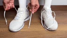 Close up of a woman tying shoelaces on white sneakers indoors. Sport shoes on wooden floor. Preparing for workout, fitness, jogging, training or daily casual activity. - Powered by Shutterstock - Get 15% off with code: PIKWIZARD15