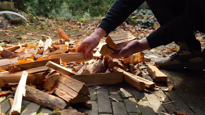 Chopped firewood for the stove. Mens hands collect firewood for heating the house.A man prepares firewood on a terrace covered with autumn leaves. Heating season. Solid natural heating fuel. 4k