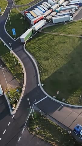 escort tight roundabout, aerial shot capturing precise truck maneuvering, wide aerial view displaying truck executing challenging tight turn between trailers with precision navigation