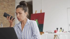 Woman talking into phone at laptop in art studio, network icons radiating across frame to connect. Mature, home, workspace, easel, canvas, paint, brushes - Powered by Shutterstock - Get 15% off with code: PIKWIZARD15