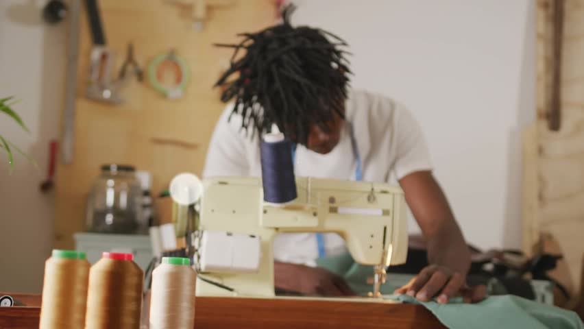 Tailor guiding fabric at machine for fashion, animated network icons fading in overlaying work area. Sewing, studio, workshop, spools, pegboard, measuring, textile