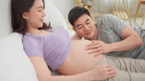 Asian husband and pregnant wife lying together on cozy bed in bedroom. Attractive expectant couple gently touching her baby bump with love and joy, ready to become parents in the near future at home. - Powered by Shutterstock - Get 15% off with code: PIKWIZARD15