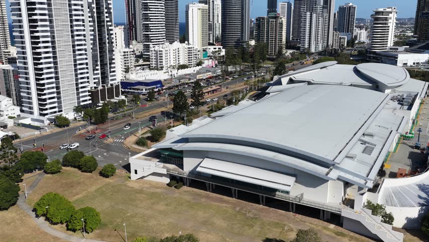 Daytime drone footage glides above convention center, revealing Gold Coast skyscrapers, coastline, and highway