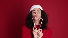 Beautiful woman with Santa hat and candy canes on red background. Christmas season - Powered by Shutterstock - Get 15% off with code: PIKWIZARD15
