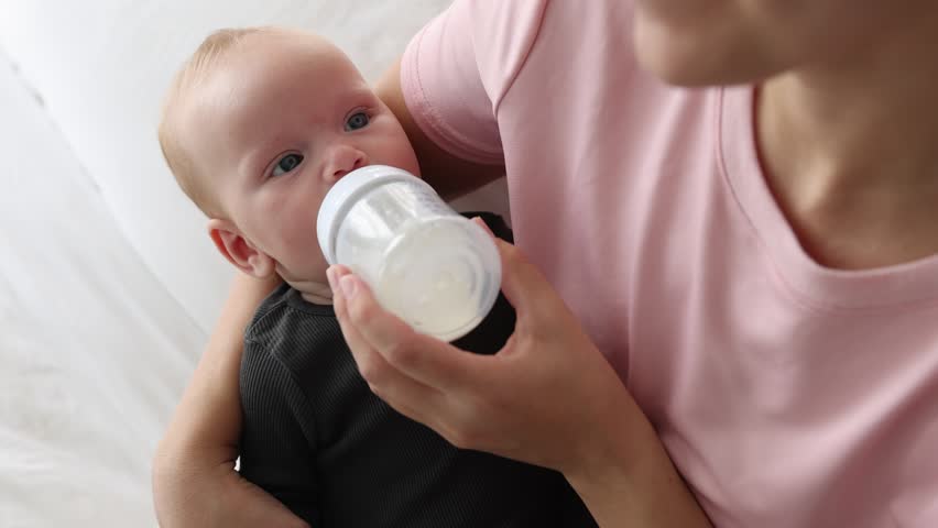 Mother feeding her little baby with bottle at home, above view