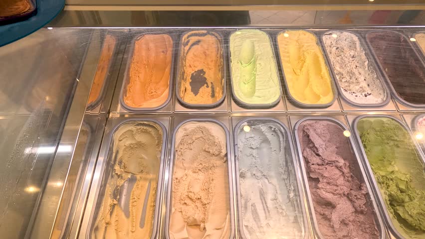 Overhead view of assorted gelato flavors in a well-lit dessert shop display counter