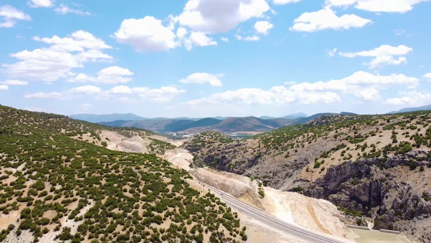 Aerial view of a stunning mountain valley landscape near Fethiye, Turkey, featuring rolling hills covered in sparse vegetation, a winding road or path through the valley, and a clear blue sky with sca