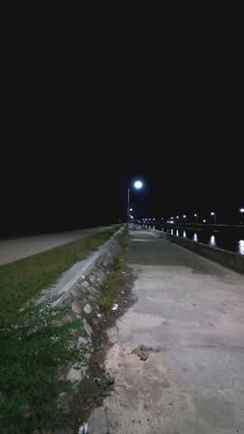 People Cycling Along the Sidewalk at Night. A man cycling on the sidewalk at night in a quiet village