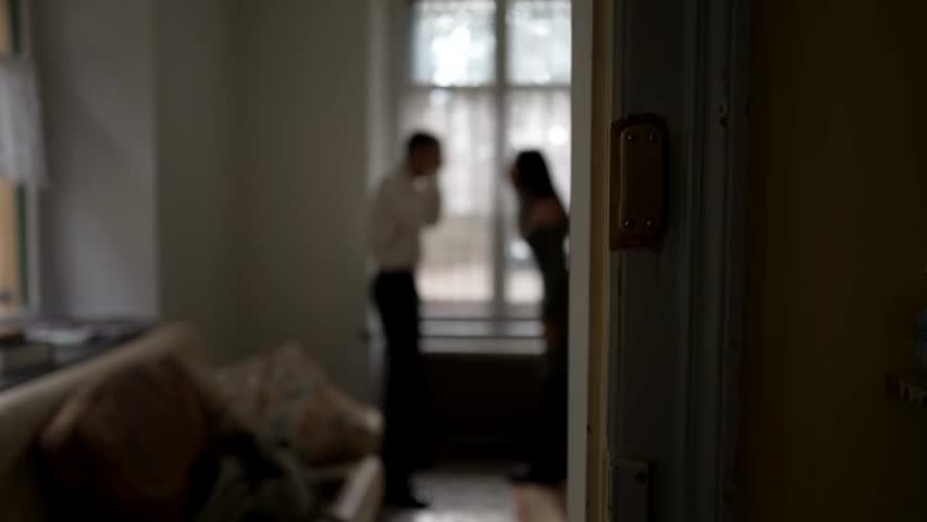 A blurred candid shot of a couple arguing at home, capturing tense body language, emotional conflict, and an intense domestic moment in a private setting.