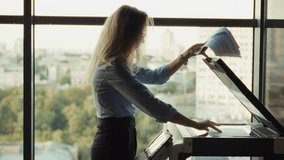 Woman Reading Documents By Office Window, Female Professional With Paperwork At Printer, Corporate Executive Analyzing Reports. Copy Machine Usage, Document Management. Professional Attire Office Day - Powered by Shutterstock - Get 15% off with code: PIKWIZARD15