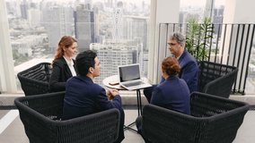 Two business professionals shake hands outdoors on a rooftop, while colleagues sit nearby with a laptop. The group engages in a collaborative meeting with a city skyline in the background. 4k video - Powered by Shutterstock - Get 15% off with code: PIKWIZARD15