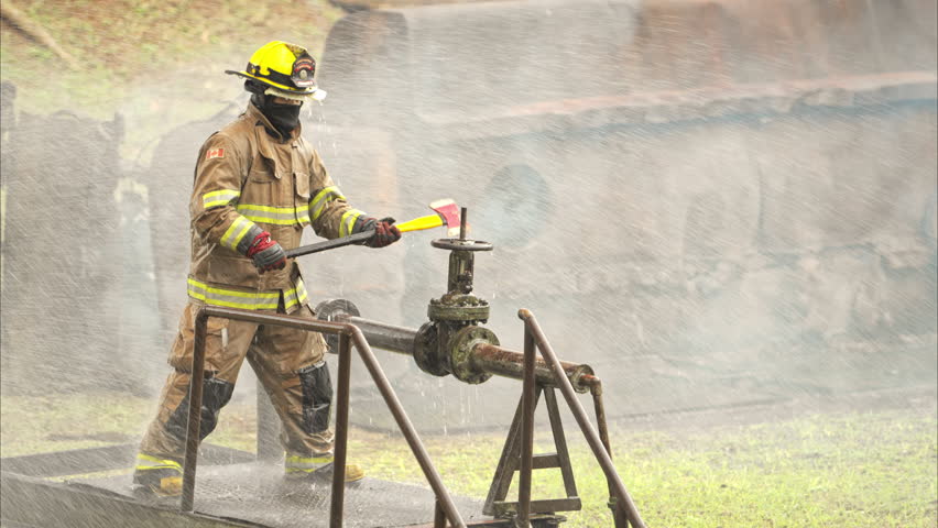 A firefighter in protective gear swings an axe while performing an emergency response in fire hydrant valve. Water sprays through the air as the firefighter works under hazardous conditions