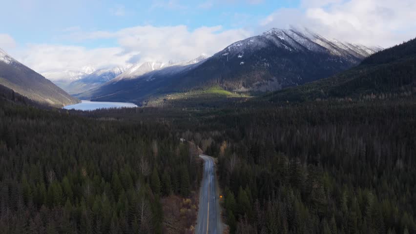 Winding Road Through Lush Forest Towards Lake and Snow-Capped Mountains in British Columbia, Canada