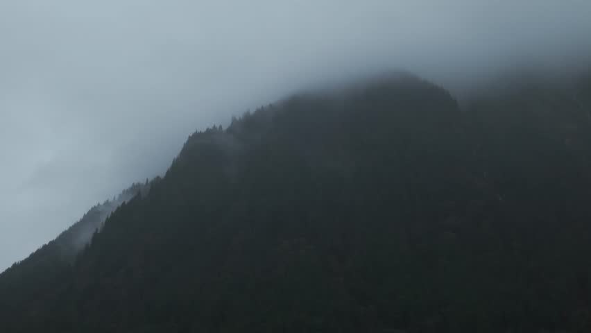 Wide dolly aerial shot of waterfalls running down misty mountains during rainy fall weather in Juneau, Alaska. 4K