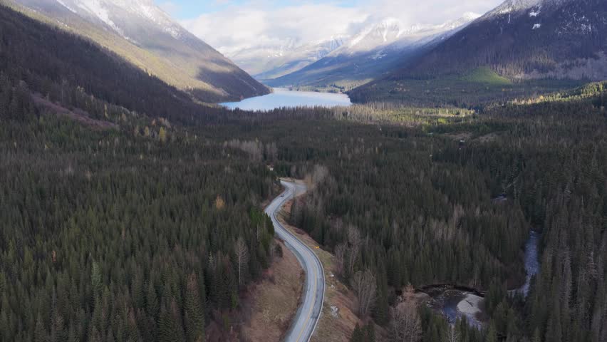 Winding Road Through Forest Leads to Lake and Snow-Capped Mountains in British Columbia, Canada