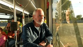 Pensive senior man with a gray beard traveling on public transport, looking thoughtfully out the window at the passing city with his reflection visible on the glass during a sunny day - Powered by Shutterstock - Get 15% off with code: PIKWIZARD15