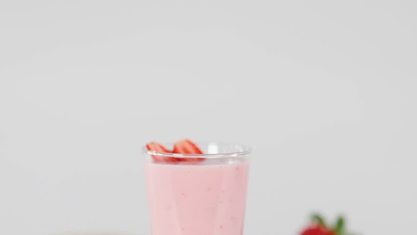 Red swirly straw inserted into creamy strawberry milkshake, bright lighting, colorful fresh fruit background