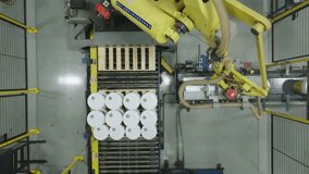 Top-down aerial shot of a yellow robotic arm performing palletizing by stacking white pails buckets onto a wooden pallet on an automated production line. - Powered by Shutterstock - Get 15% off with code: PIKWIZARD15