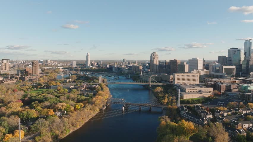Cinematic aerial drone flight over the Hennepin Avenue Bridge and Mississippi River during fall golden hour, showcasing the Minneapolis, MN skyline.